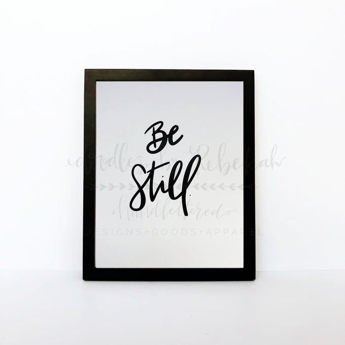 An 8x10 framable print with the phrase 'BE STILL' in a cursive handwritten style font, predominantly in black color.
