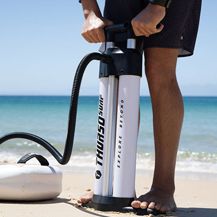Person using a Thrurso paddleboard pump on a beach with ocean in the background